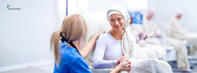 Pflegefachkraft hält die Hand einer Patientin während einer Zytostatika-Infusion und spricht beruhigend mit ihr